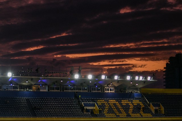 Stadionske tribine osvetljene reflektorima ispred slojevitih tamnoružičastih oblaka
